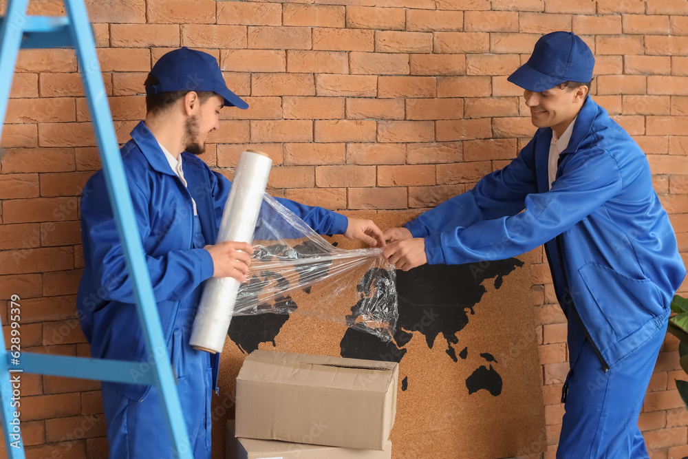 Male movers wrapping world map with stretch film in room