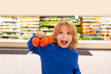 Child with fresh tomato vegetables. Child at vegetable supermarket. Little kid choosing food in store or grocery store.