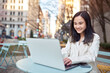 © insta_photos - Young smiling Asian business woman professional or student on city street at table using laptop working or elearning on computer tech connected online for work, education and communication.