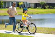 Father And Son In Bike Helmet For Learning To Ride Bicycle At Park. Father Helping Son Cycling. Father And Son On The Bicycle On Summer Day. Little Son Trying To Ride Bike With Father. Fathers Day.