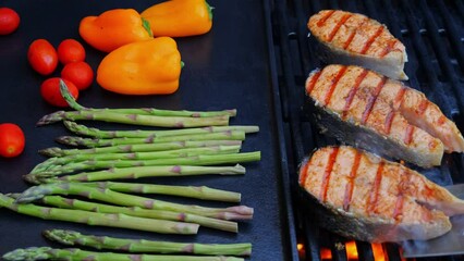 Wall Mural - cooking grilled fish steak salmon with asparagus, tomato, pepper on grill, close up, outdoor