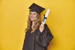 © Asier - Young caucasian woman wearing a graduation robe holding a diploma Ylooks aside smiling, cheerful and pleasant.