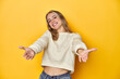 © Asier - Young blonde Caucasian woman in a white sweatshirt on a yellow studio background, showing a welcome expression.