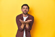 © Asier - Caucasian man in red checkered shirt, yellow backdrop folding lips and holding palms to send air kiss.