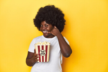 Movie night concept with woman holding popcorn showing a mobile phone call gesture with fingers.