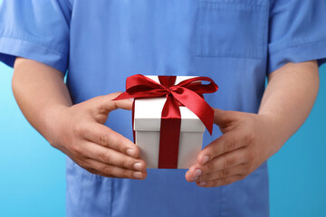 Wall Mural - Doctor holding gift box on light blue background, closeup. Medical present