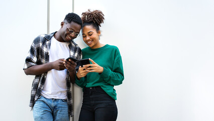 African American young couple looking smart phones together standing against white wall. Copy space.