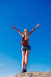 © M.studio - Woman standing on cliff with open arms against blue sky- freedom,  achievement,