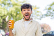 Young Arabian handsome man holding an orange juice at outdoors with surprise and shocked facial expression