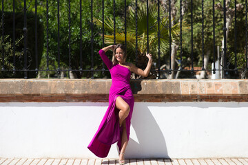 Pretty young blonde woman in a purple dress leaning against a park fence making different body expressions while posing for photos. Beauty and fashion concept.