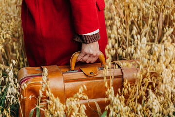 Sticker - Closeup view on woman in red coat hold vintage suitcase in oat field