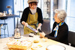 © Monet - 顧客のシニア女性にタッチレス決済を案内するカフェ店員