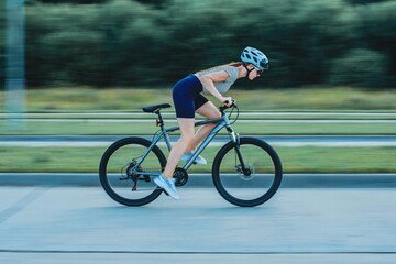 sports girl in a bicycle helmet and glasses rides a bicycle photo in motion, blurred background