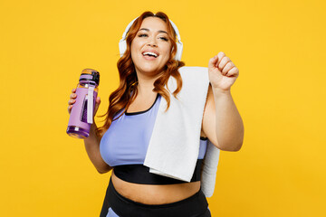 Young fun chubby overweight plus size big fat fit woman wear blue top warm up train listen to music in headphones drink water isolated on plain yellow background studio home gym Workout sport concept