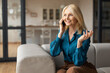 © Prostock-studio - Cheerful mature woman talking on phone looking aside and smiling, sitting on couch at home, having pleasant mobile call