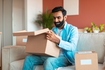 Wall Mural - Happy Middle Eastern customer man opening cardboard boxes at home