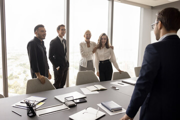 Sticker - Cheerful business team and business leader standing at large meeting table in boardroom, talking, laughing, enjoying teamwork. Elder businesswoman introducing new younger employee to colleagues