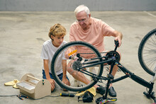 Senior Man Repairing Bicycle Wheel With Grandson