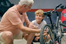 Senior Man Explaining Mechanism Of Bicycle To Grandson