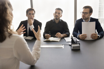 Canvas Print - Rear view of job candidate woman speaking to HR team on interview meeting. Employers listening to vacancy applicant, discussing work experience, career growth opportunity