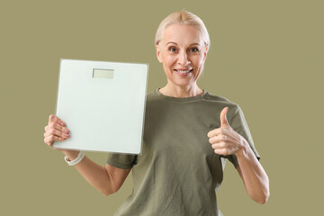 Poster - Sporty mature woman with scales showing thumb-up on green background