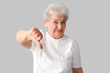 Wall Mural - Displeased senior woman showing thumb-down on grey background