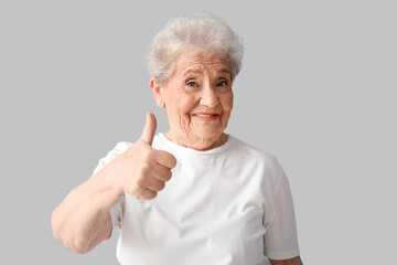 Wall Mural - Senior woman showing thumb-up on grey background