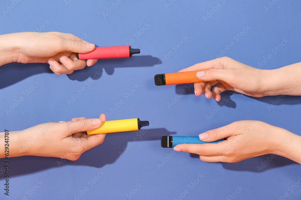 Women holding electronic cigarettes on blue background
