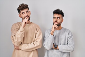 Wall Mural - Young homosexual couple standing over white background with hand on chin thinking about question, pensive expression. smiling and thoughtful face. doubt concept.