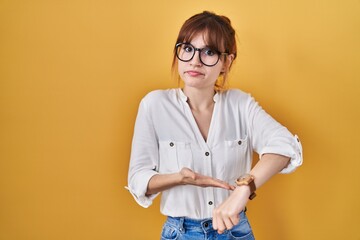 Wall Mural - Young beautiful woman wearing casual shirt over yellow background in hurry pointing to watch time, impatience, upset and angry for deadline delay