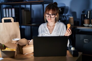 Canvas Print - Young beautiful woman working using computer laptop and eating delivery food skeptic and nervous, frowning upset because of problem. negative person.