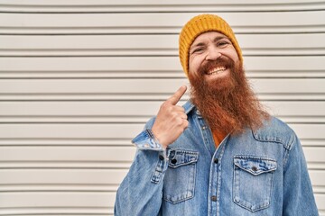 Wall Mural - Caucasian man with long beard waring wool hat smiling happy pointing with hand and finger