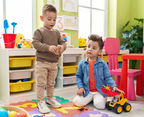 Wall Mural - Adorable boys playing with tractor and dinosaur toy sitting on floor at kindergarten