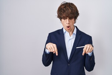 Canvas Print - Hispanic business young man wearing glasses pointing down with fingers showing advertisement, surprised face and open mouth