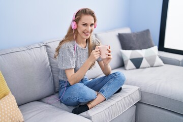 Poster - Young blonde woman listening to music drinking coffee at home