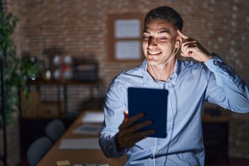 Wall Mural - Handsome hispanic man working at the office at night smiling pointing to head with one finger, great idea or thought, good memory