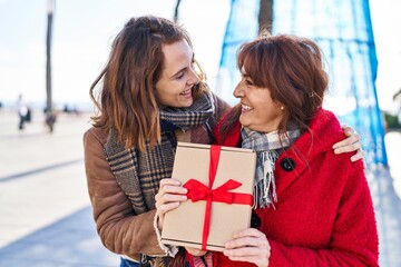 Poster - Two women mother and daughter hugging each other surprise with gift at street