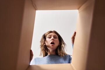 Canvas Print - Beautiful woman opening cardboard box afraid and shocked with surprise and amazed expression, fear and excited face.