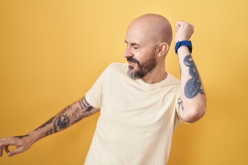 Poster - Hispanic man with tattoos standing over yellow background dancing happy and cheerful, smiling moving casual and confident listening to music