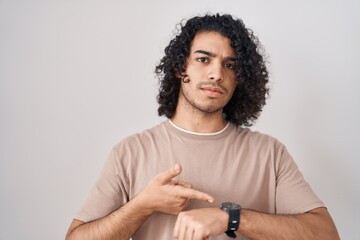 Sticker - Hispanic man with curly hair standing over white background in hurry pointing to watch time, impatience, upset and angry for deadline delay