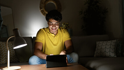 Sticker - Young latin man using touchpad sitting on sofa at home