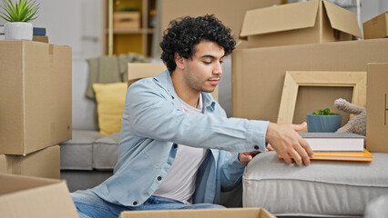 Poster - Young latin man packing cardboard box holding books at new home