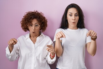 Wall Mural - Hispanic mother and daughter wearing casual white t shirt over pink background pointing down with fingers showing advertisement, surprised face and open mouth