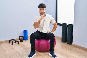 Sticker - Hispanic man with beard sitting on pilate balls at yoga room asking to be quiet with finger on lips. silence and secret concept.