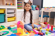 © Krakenimages.com - Adorable hispanic girl playing with construction blocks sitting on floor at kindergarten