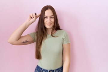 Canvas Print - Beautiful brunette woman standing over pink background smiling pointing to head with one finger, great idea or thought, good memory