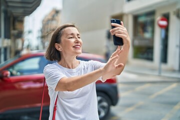 Wall Mural - Middle age woman smiling confident making selfie by the smartphone at street