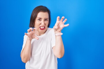 Wall Mural - Middle age hispanic woman standing over blue background smiling funny doing claw gesture as cat, aggressive and sexy expression