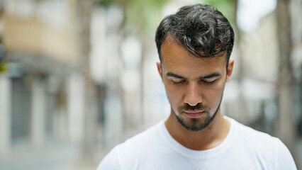 Wall Mural - Young hispanic man looking down with serious expression at street