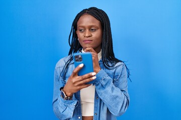 Sticker - African woman with braids using smartphone typing message serious face thinking about question with hand on chin, thoughtful about confusing idea